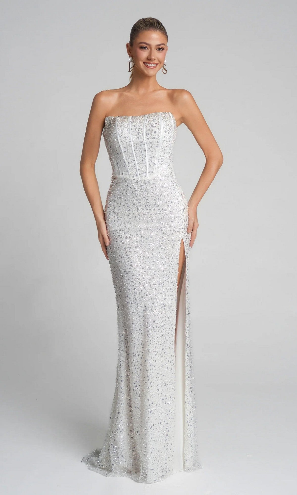 A woman wears the Portia and Scarlett XO054 long formal dress in ivory—strapless, floor-length, covered in sequins, with a thigh-high slit and corset bodice—standing against a plain light background.